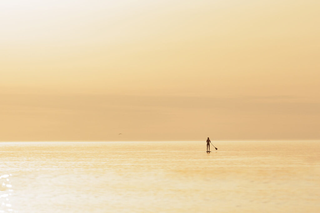 Urlaubsplanung 2025 Frau auf StandUp Paddle im goldenen Sonnenuntergang